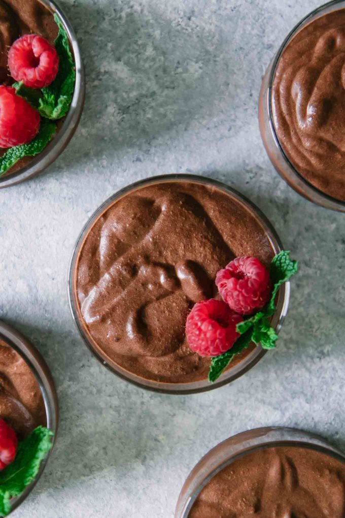 bowls of chocolate mousse with raspberry and mint garnish on a white table