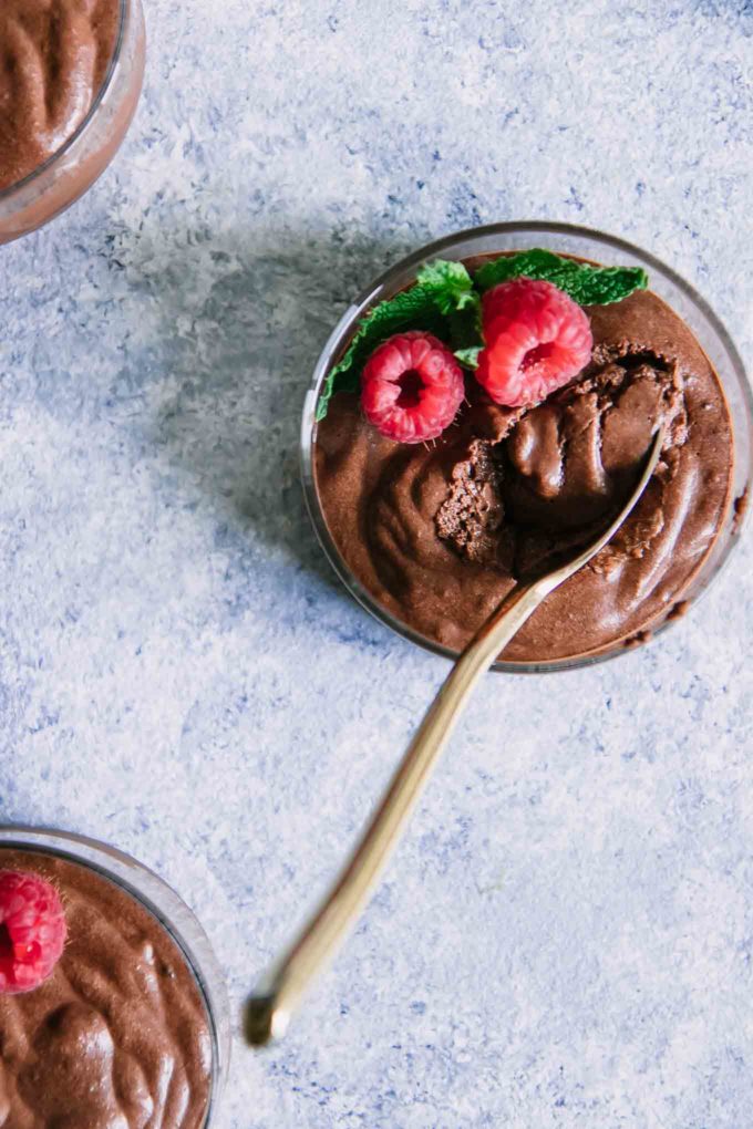 a small bowl of chocolate mousse with a gold spoon dipped in on a blue table
