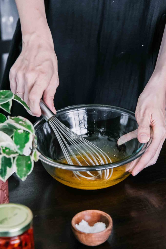 a hand whisking salad dressing in a glass mixing bowl on a wooden table