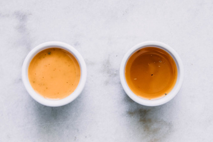 two small bowls of tomato vinaigrette dressings on a white table, one dressing is a darker color because it was blended and another is lighter and more oily
