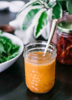 a mason jar with orange salad dressing and a gold spoon on a wooden table