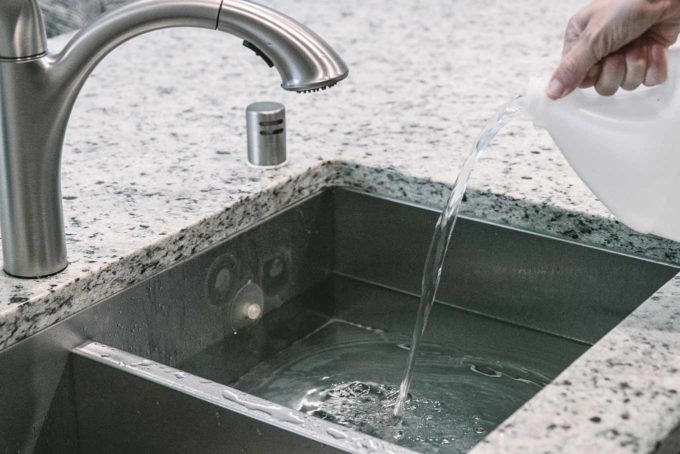 a hand pouring white distilled vinegar into a sink filled with water