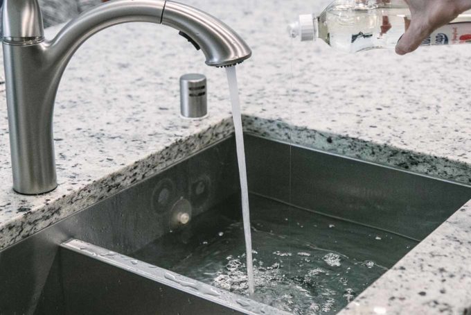 a hand pouring dish soap into a kitchen sink filled with water