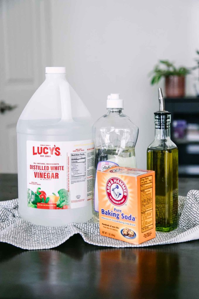 bottles of distilled white vinegar, dish soap, oil, and baking soda on a wooden table
