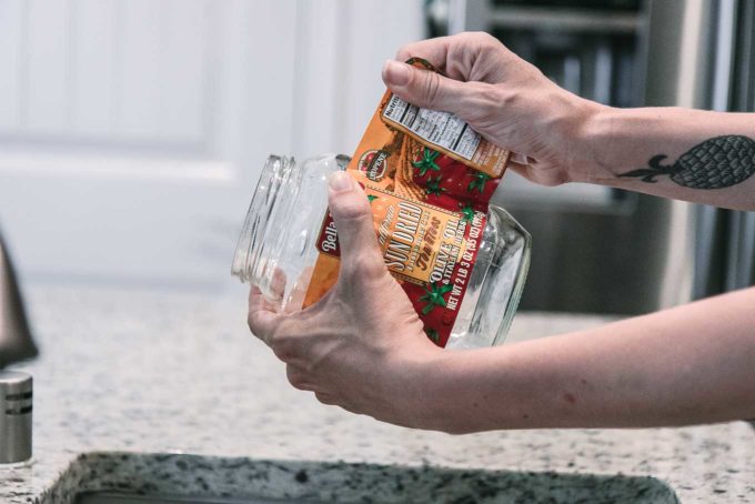 a hand peeling a label from an empty glass food jar