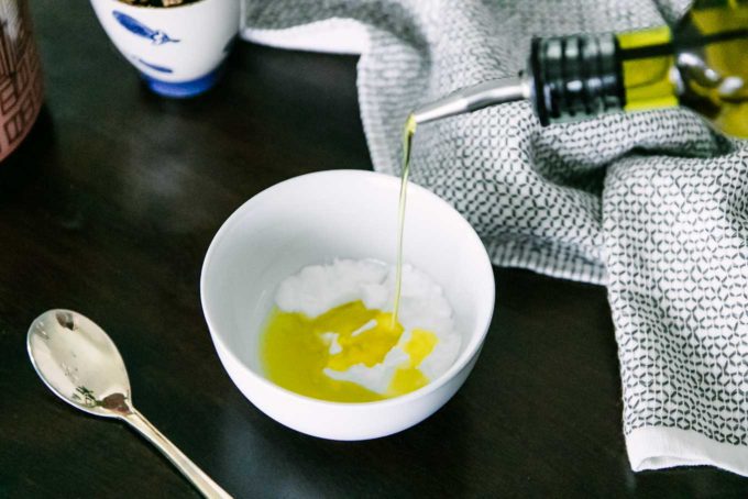 oil pouring into a small white bowl filled with baking soda