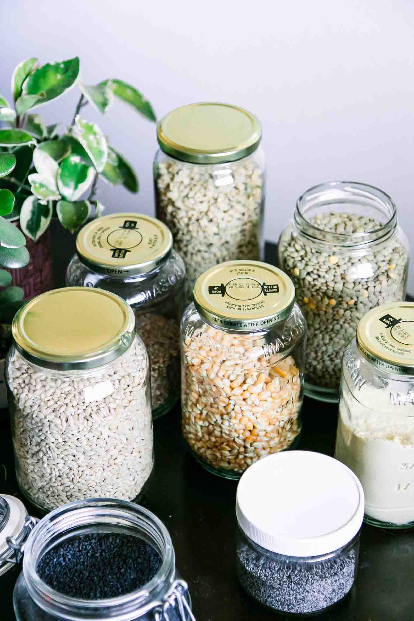 glass food jars filled with dried bulk food on a wooden table with a green plant