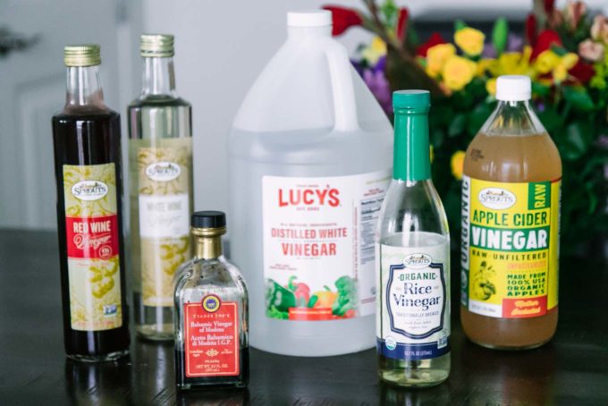 bottles of red wine, white wine, distilled, rice, apple cider, and balsamic vinegars on a wooden table