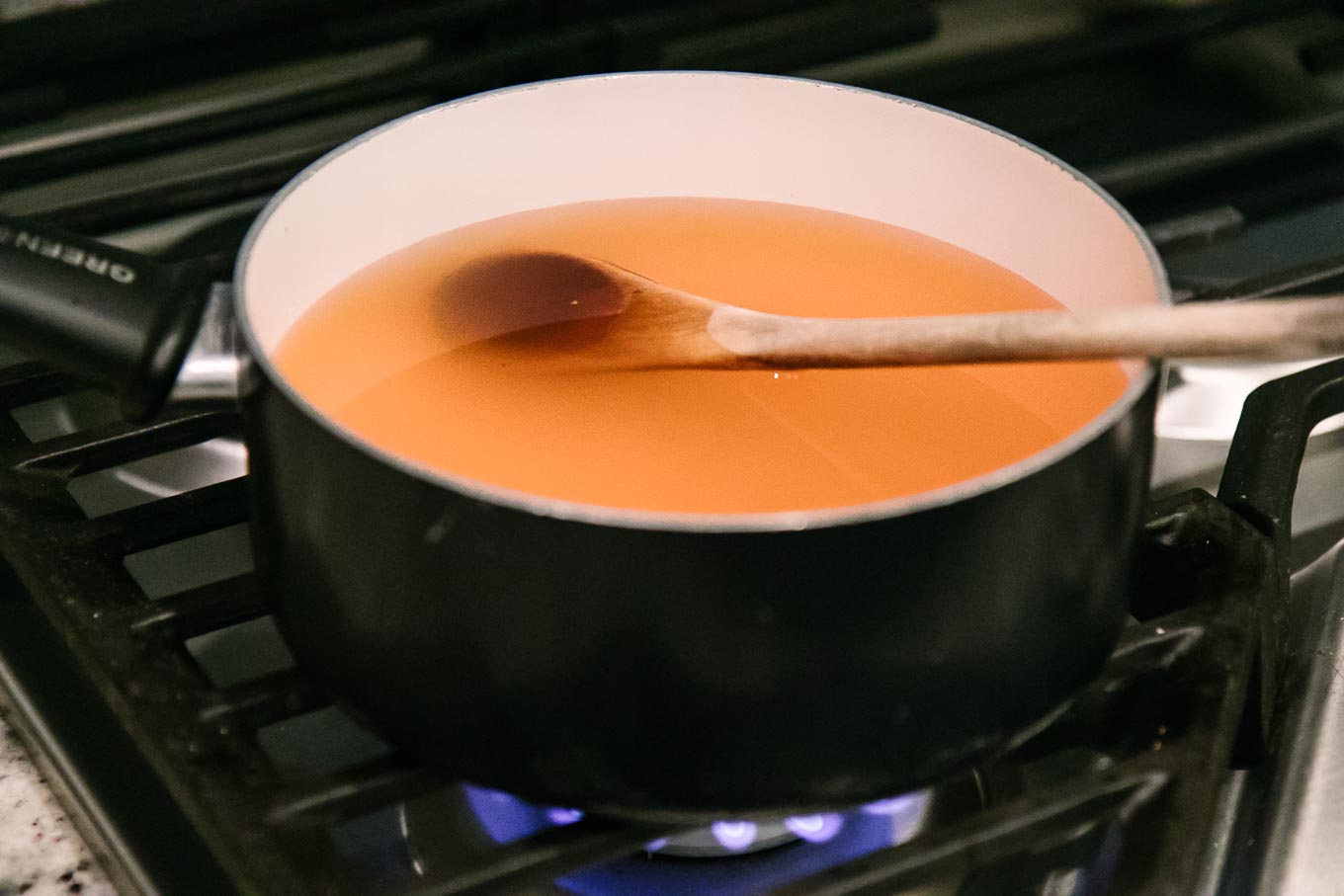 a small sauce pan filled with water and apple cider vinegar brine on a stovetop with a wooden spoon