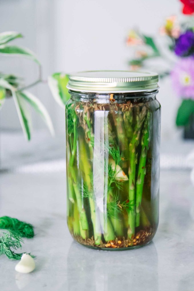 asparagus in a tall glass jar in an apple cider vinegar brine liquid on a white table