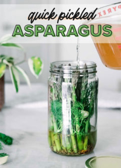 apple cider vinegar brine pouring into a tall glass jar with asparagus and herbs and the words "quick pickled asparagus" in black and green writing