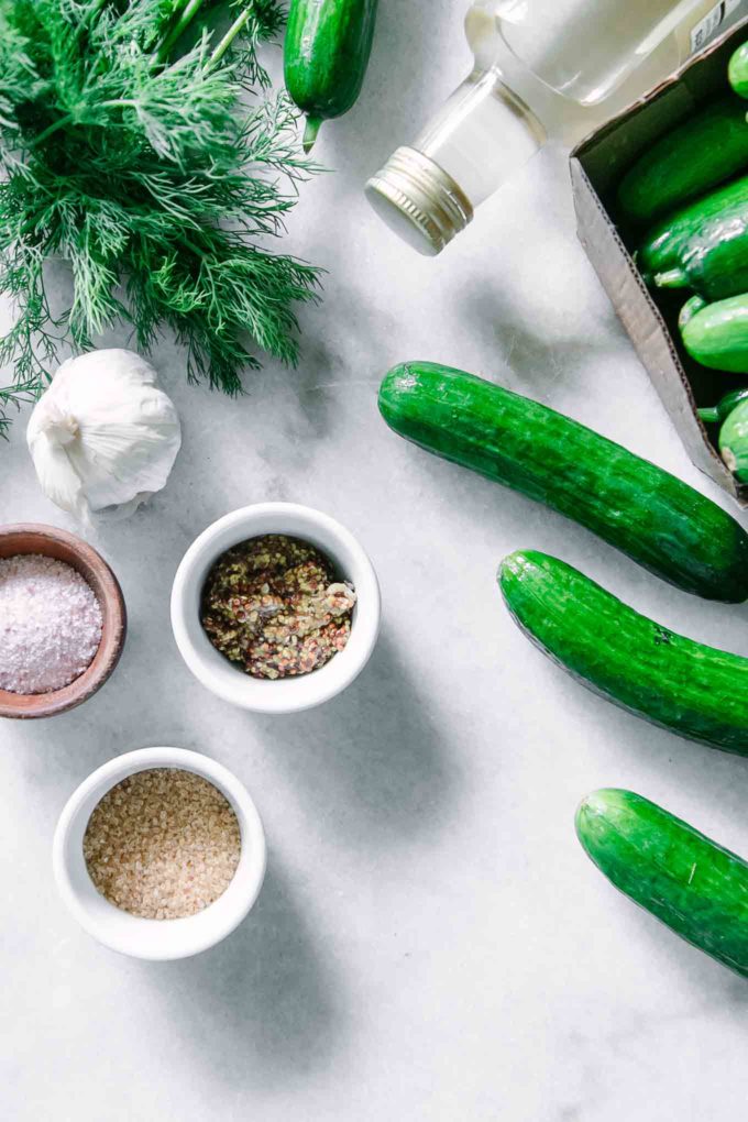persian cucumbers, fresh dill, and bowls of sugar, salt, and garlic on a white table