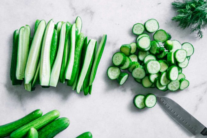cucumbers cut into spears and slices on a white table with a knife