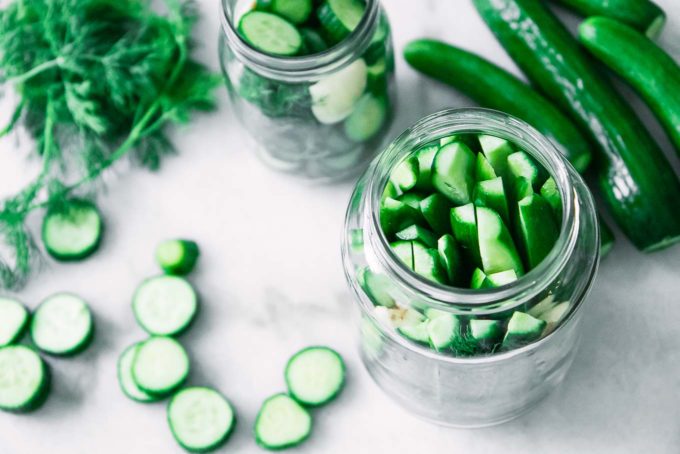 cucumber pickles in a jar with herbs and spices on a white table