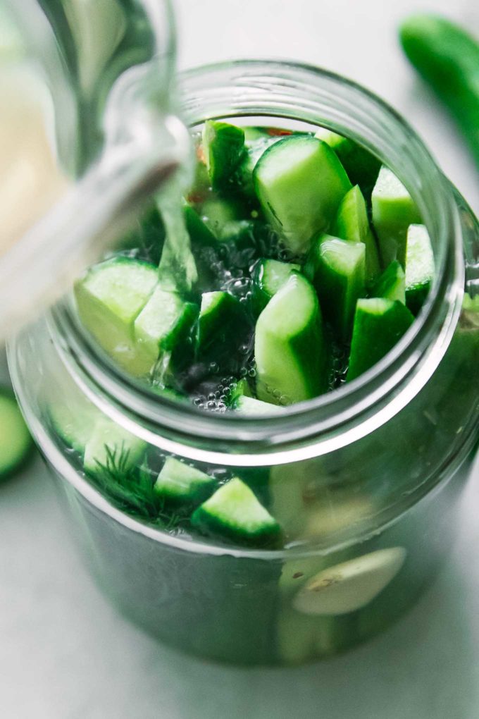 vinegar brine pouring into a jar of cut cucumbers