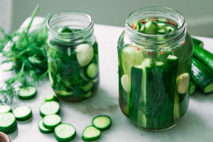 a jar of pickled cucumbers filled with vinegar on a white table