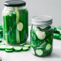 two jars of pickled cucumbers cut into spears and slices on a white table