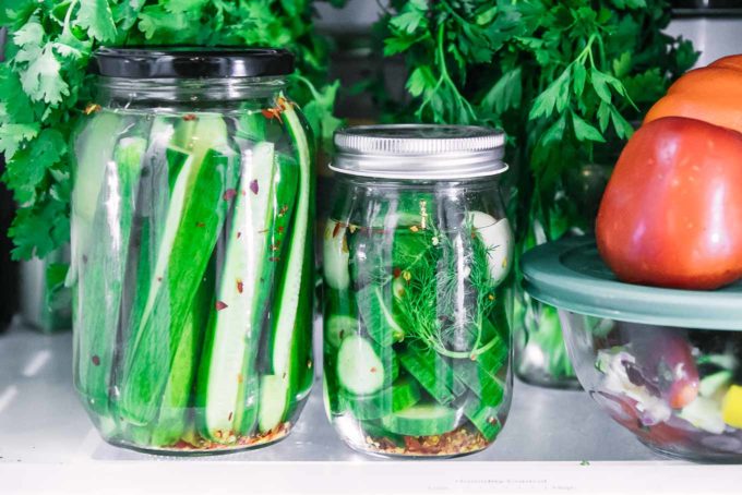 jars of cut cucumber pickles in a vinegar brine inside a refrigerator
