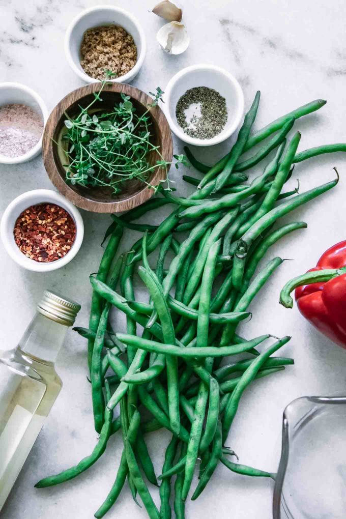 green beans, red bell pepper, garlic, thyme, red pepper, vinegar, water, salt, and sugar on a white countertop