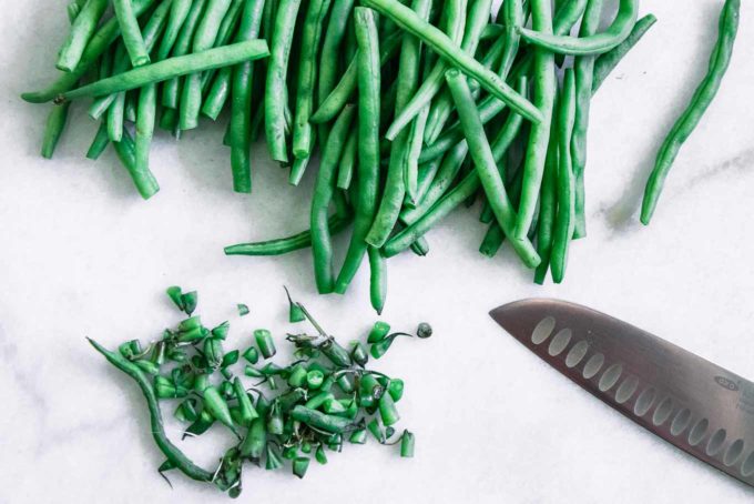 cut green beans and green bean stems on a marble countertop with a knife