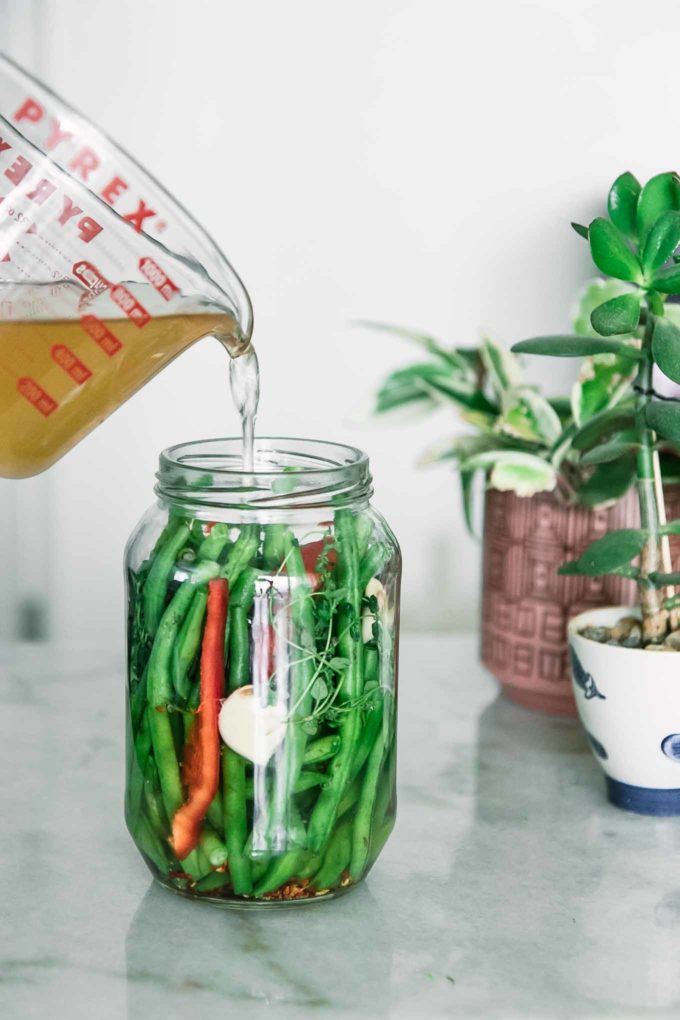 vinegar brine pouring into a jar of green beans and bell peppers