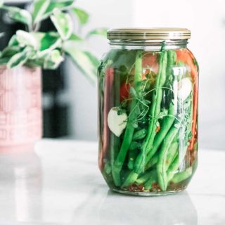 a jar of pickled green beans and bell peppers on a white table with flowers