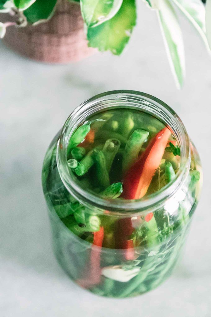 green beans and red bell pepper in a glass jar on a white table