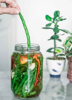 a hand pulling a green bean out of a jar on a white table