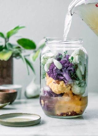 a jar of white, purple, and yellow cauliflower with a vinegar brine pouring into it