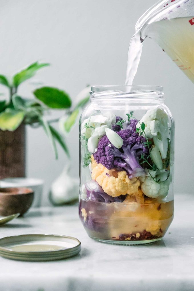a jar of white, purple, and yellow cauliflower with a vinegar brine pouring into it