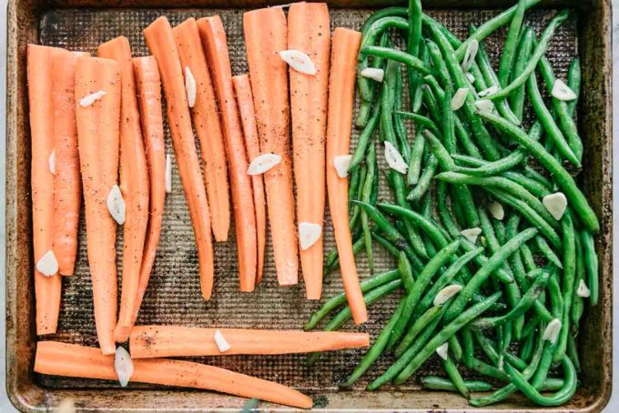 cut carrots and green beans with sliced garlic on a sheet pan