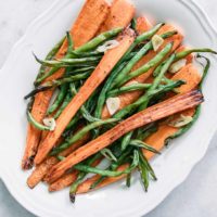 baked green beans, carrots, and garlic in a white serving dish on a white table