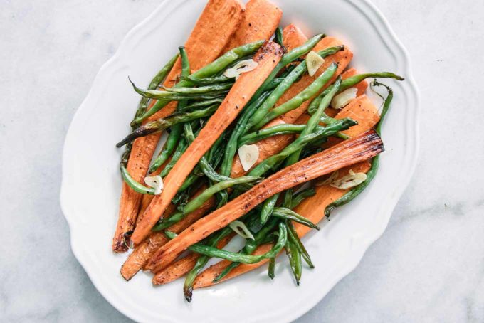 baked green beans, carrots, and garlic in a white serving dish on a white table