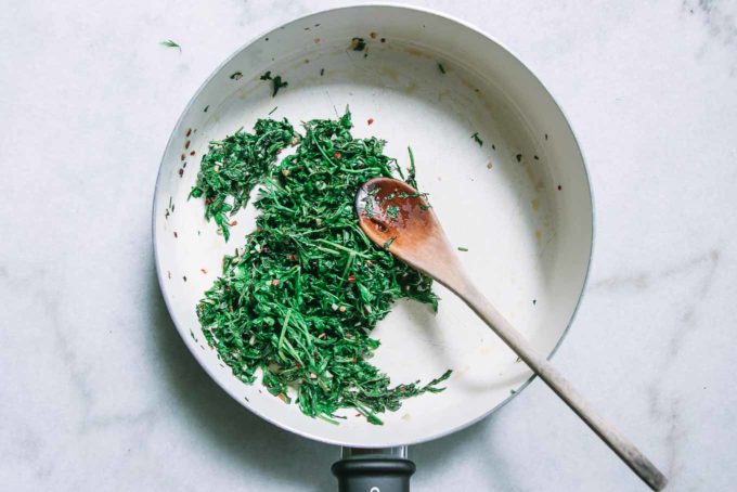 cooked carrot greens in a white pan with a wooden spoon