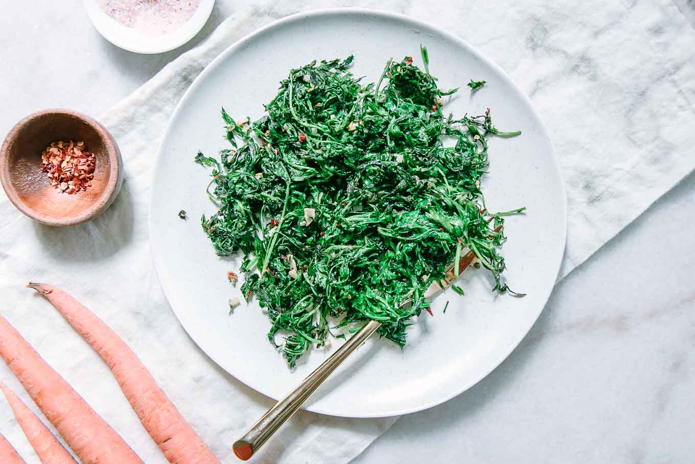 cooked carrot greens on a white plate with a gold fork