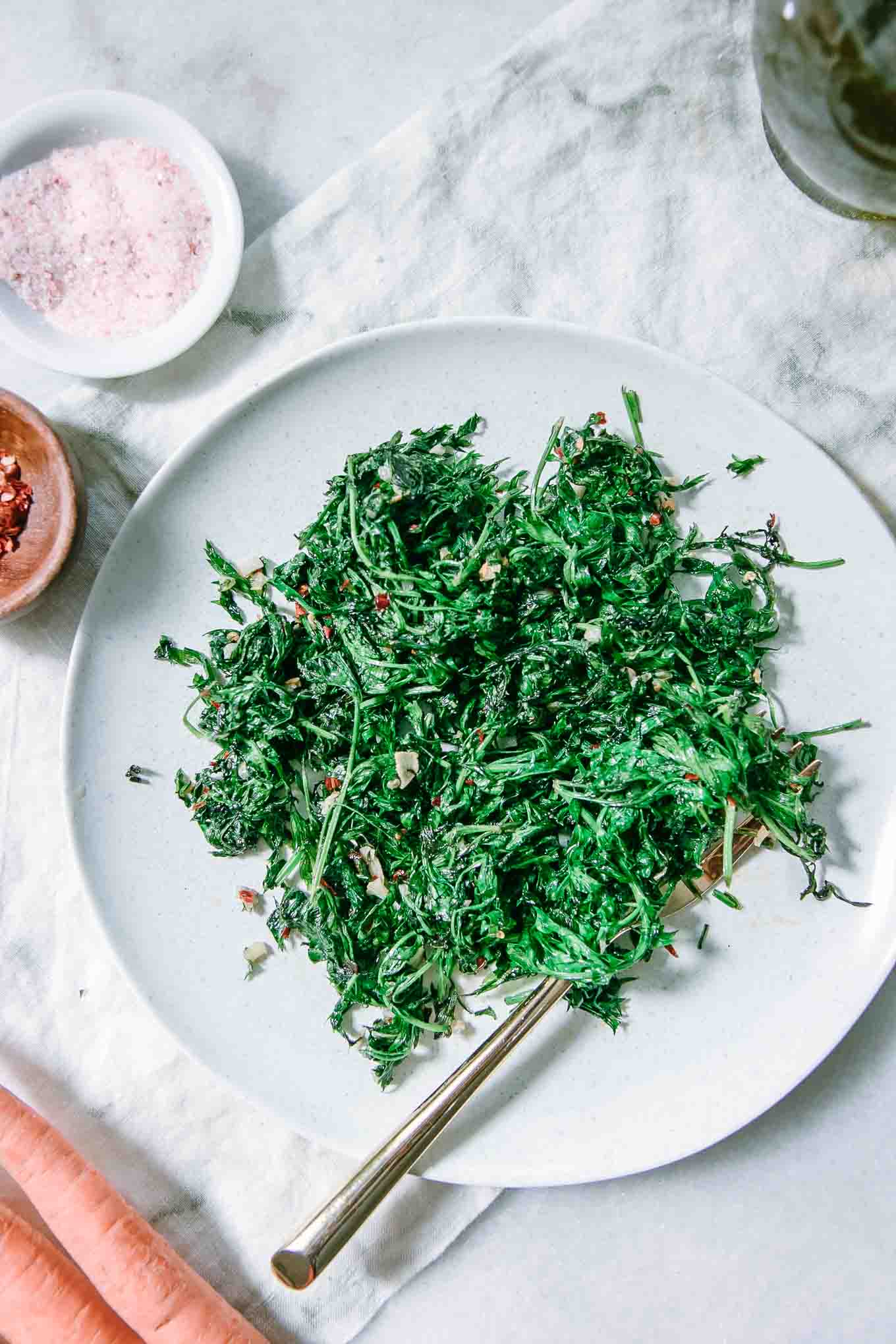 sauteed carrot leaves on top of a white plate with a gold fork on a white napkin