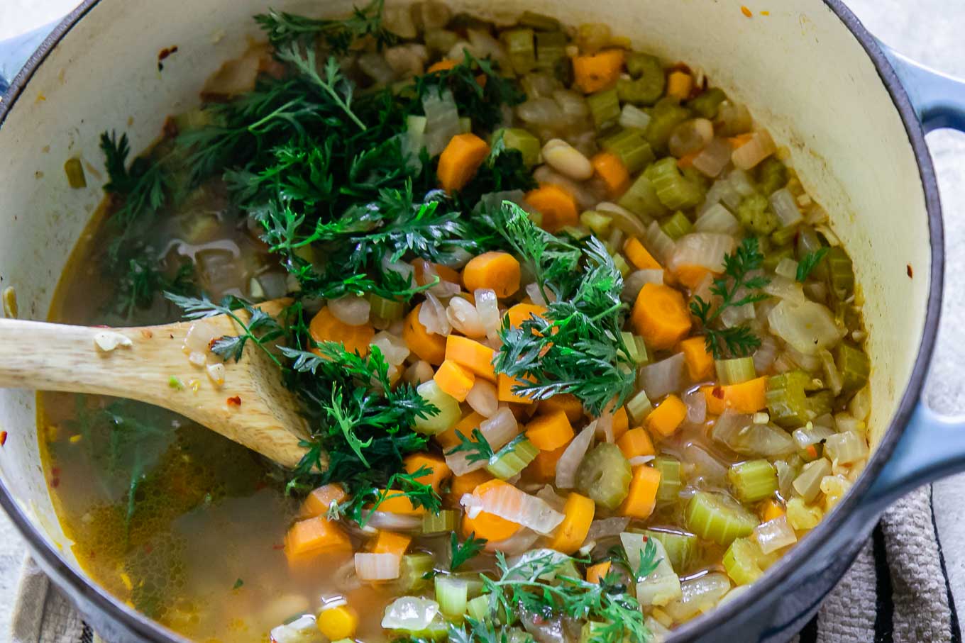 a wooden spoon stirring carrot greens into a soup