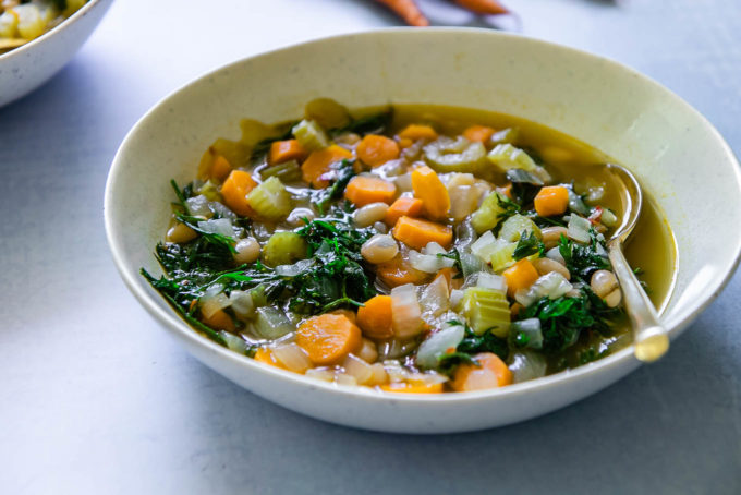 a bowl of carrot greens soup on a blue table with a gold spoon