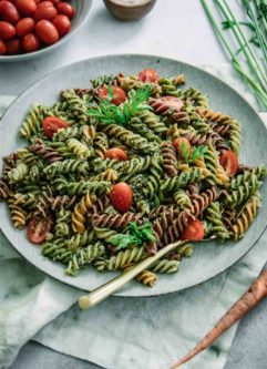 pesto pasta with cherry tomatoes on a blue plate with a gold fork