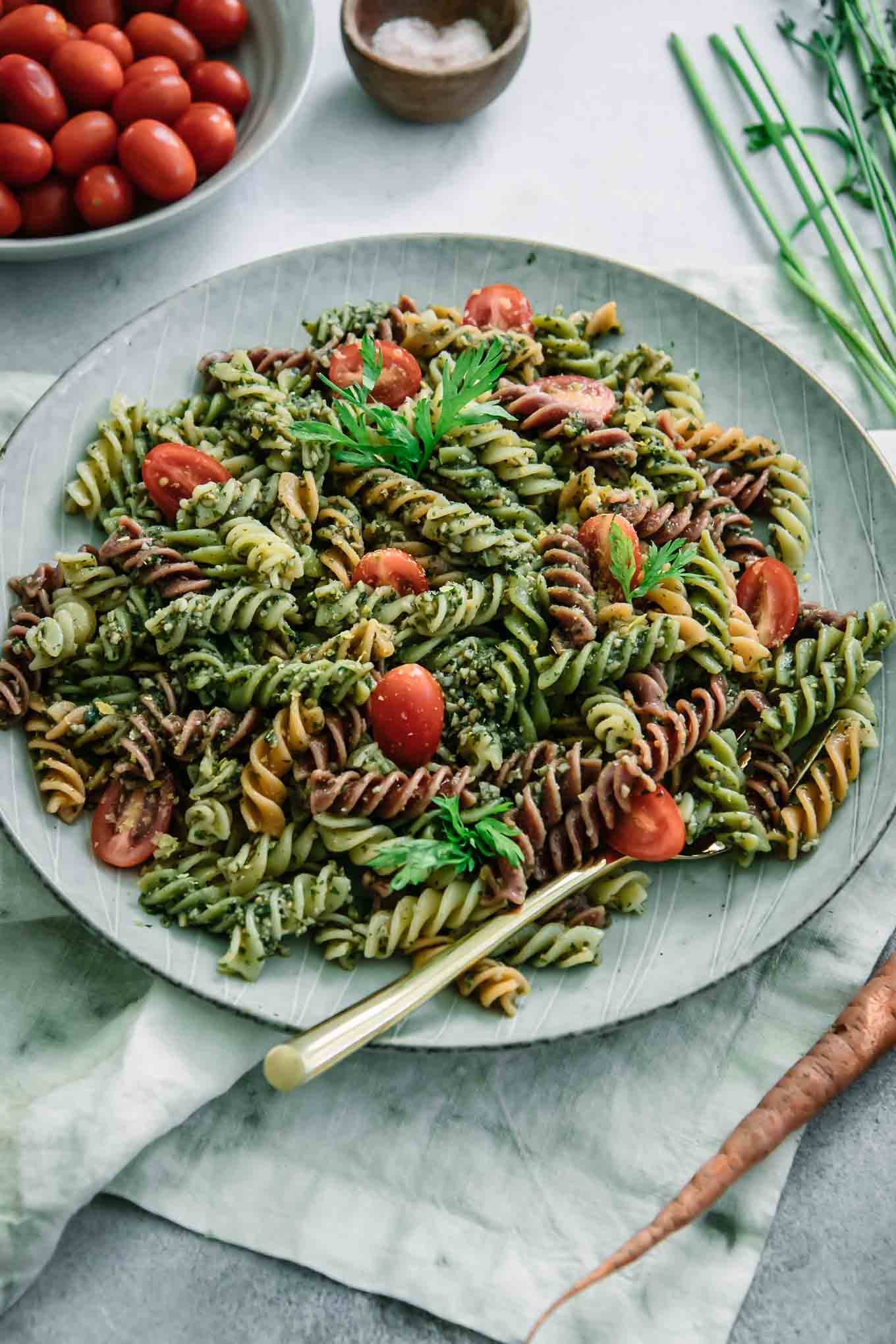 pesto pasta with cherry tomatoes on a blue plate with a gold fork