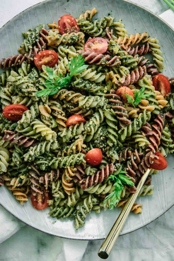 a close up photo of rotini pasta with pesto sauces and sliced red cherry tomatoes