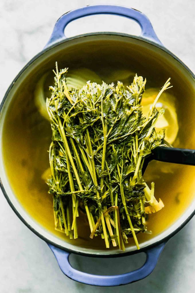 a spoon lifting carrot tops out of a soup pot