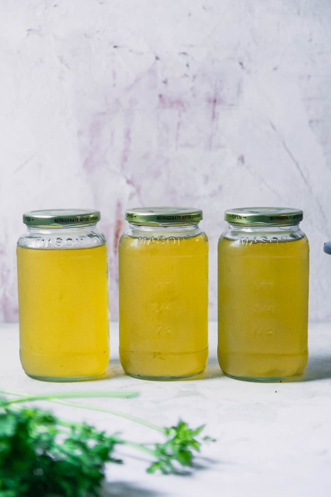 three glass jars of vegetable broth in a row on a white table