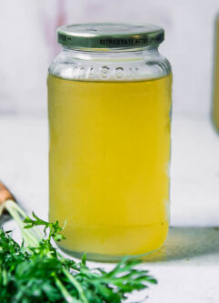 vegetable broth in a glass jar on a table with carrot greens