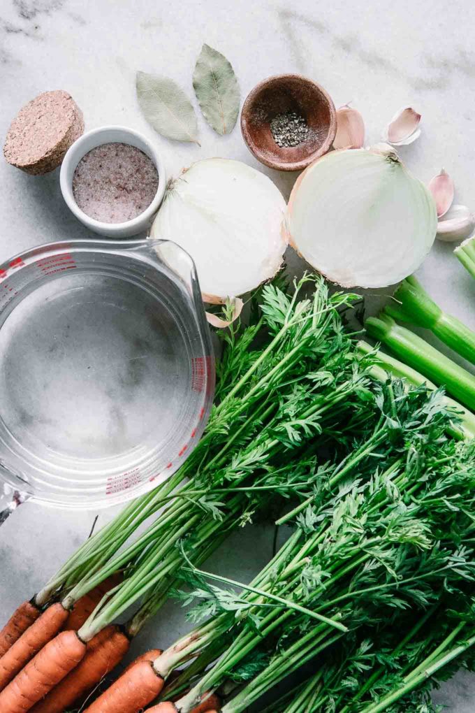 carrots with green tops, onion, salt, and a measuring cup with water on a white table