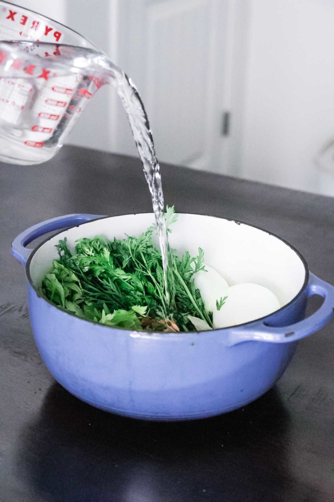 water pouring into a soup pot filled with vegetables and herbs