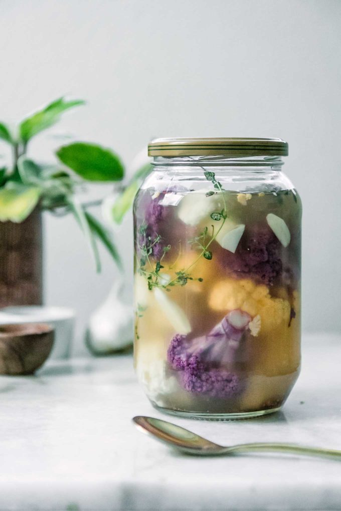 a jar of rainbow cauliflower in a pickling brine on a white table