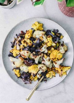 roasted white, purple, and orange cauliflower on a white plate with a gold spoon