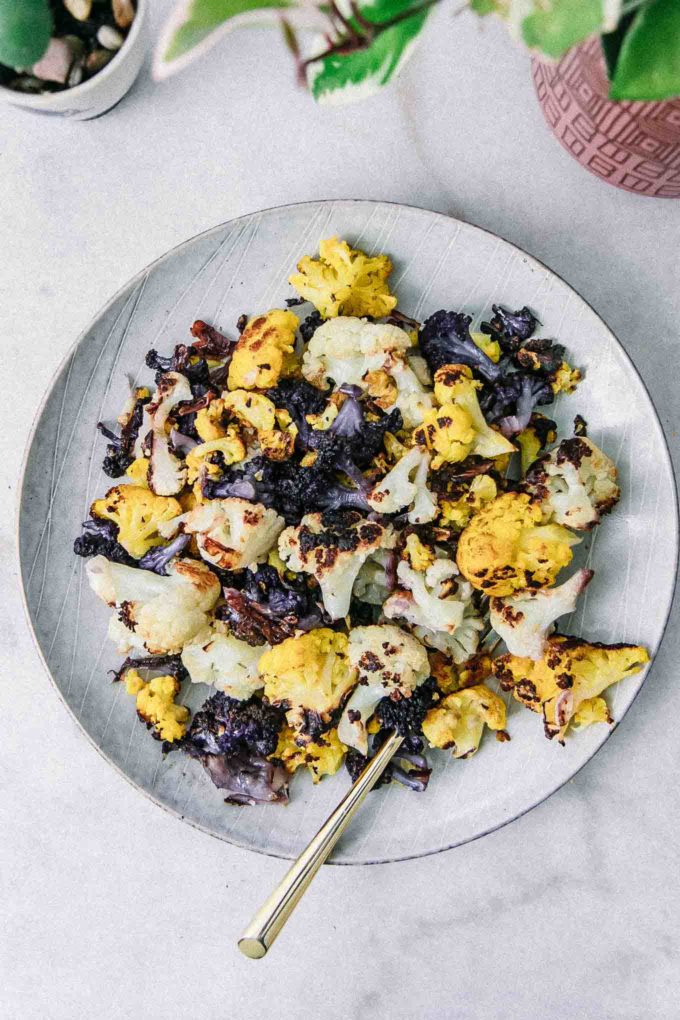 roasted white, purple, and orange cauliflower on a white plate with a gold spoon