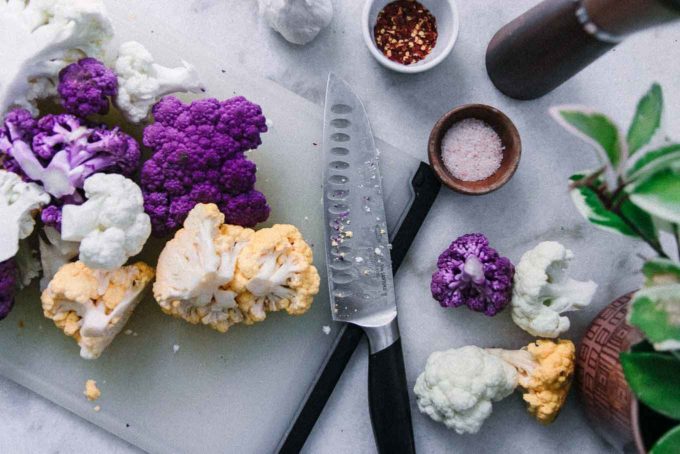 cut rainbow-colored cauliflower on a white table with a knife
